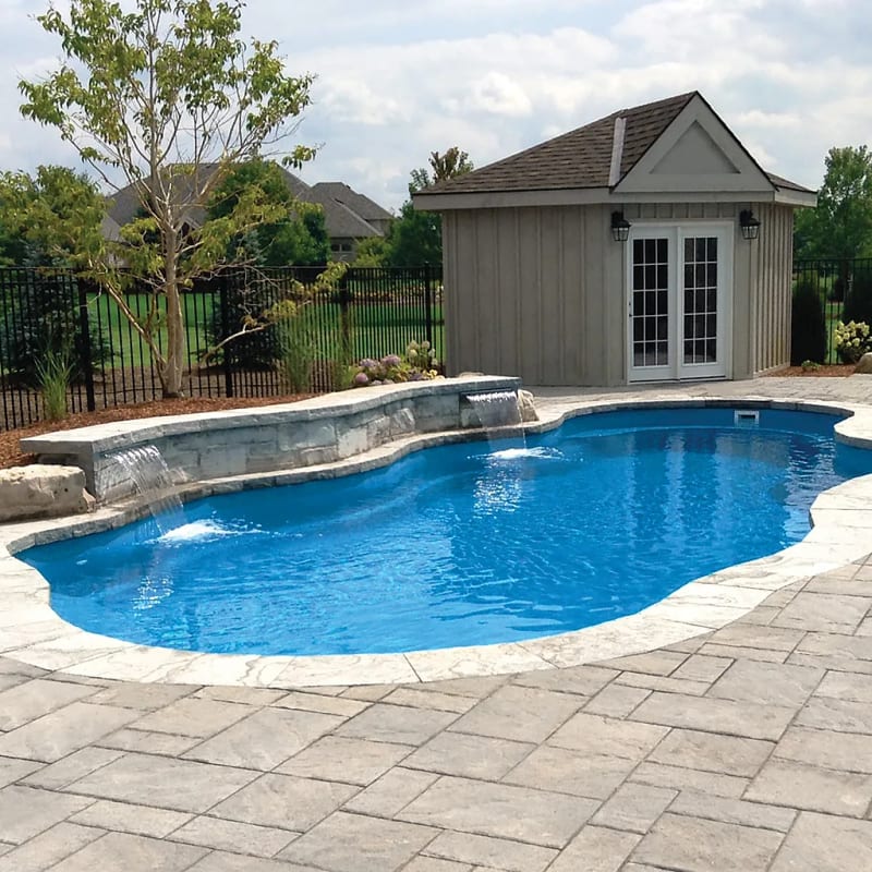 Freeform fiberglass pool with stone waterfall feature and pool house