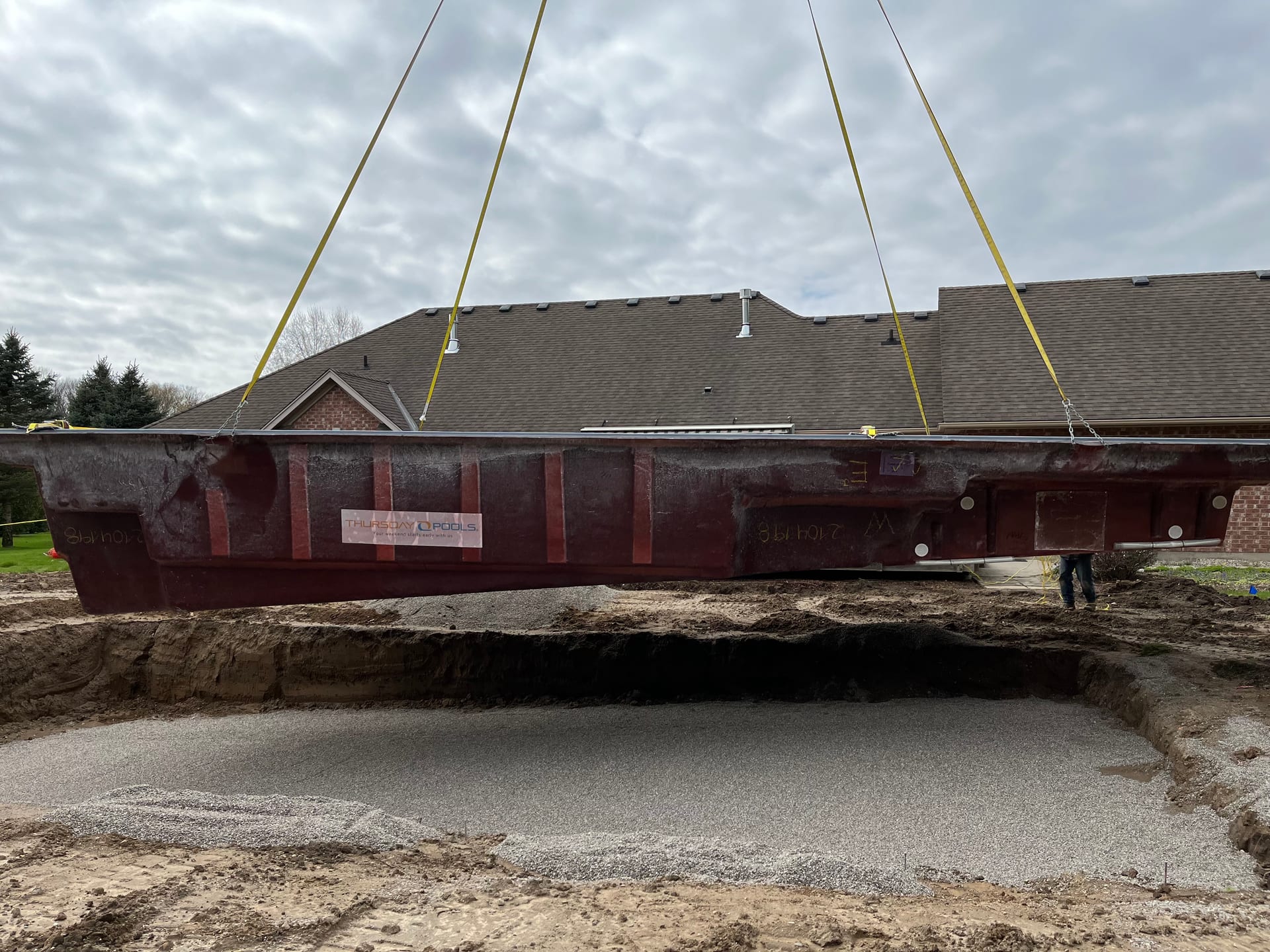 Fiberglass pool shell being crane-lowered into excavation during installation